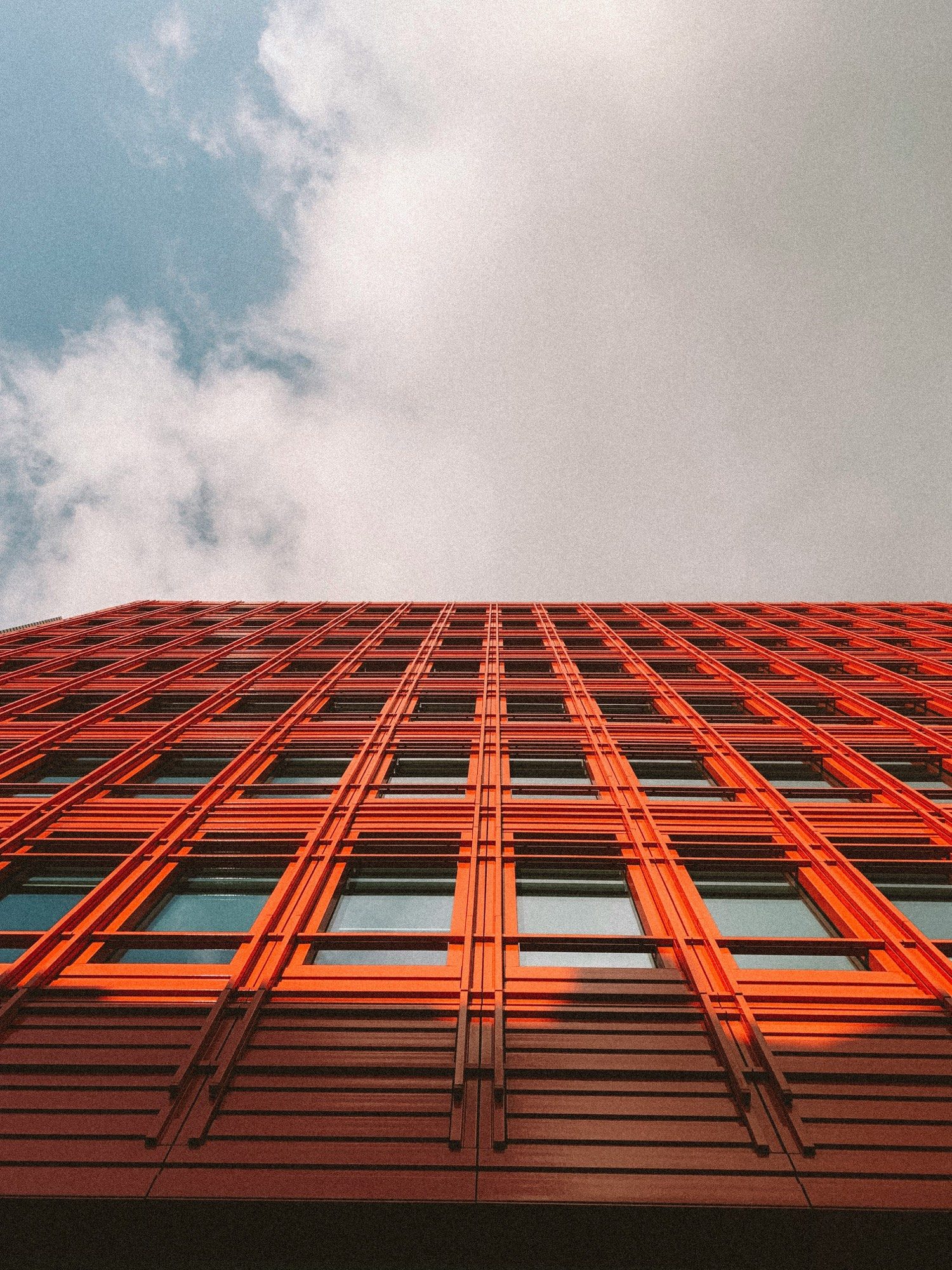 Looking up at a bold orange gridded building facade against the sky